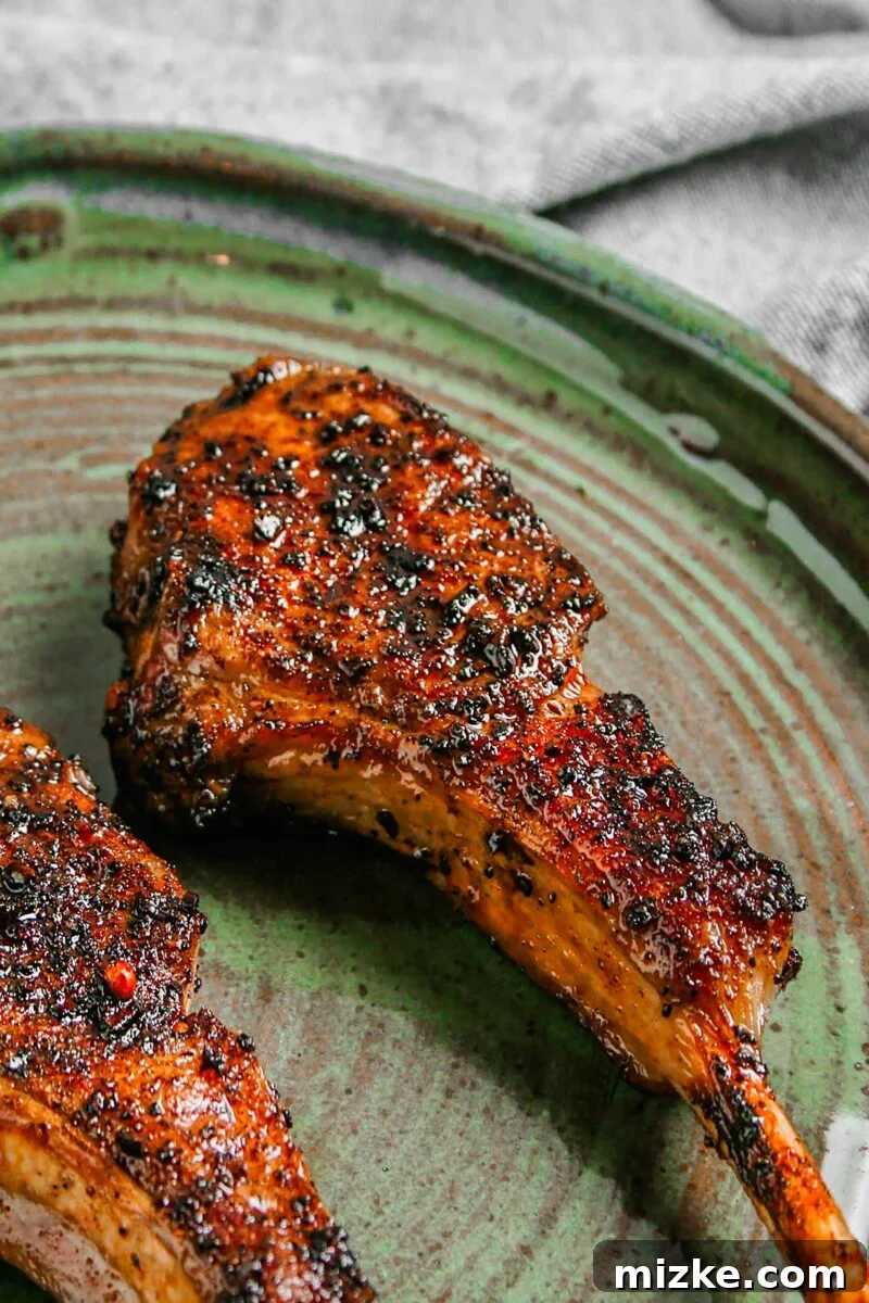 Smoky Coffee Rubbed Grilled Lamb Chops 4 Two perfectly grilled lamb chops, coated in coffee rub, are placed on a vibrant green plate with a side of fresh herbs.