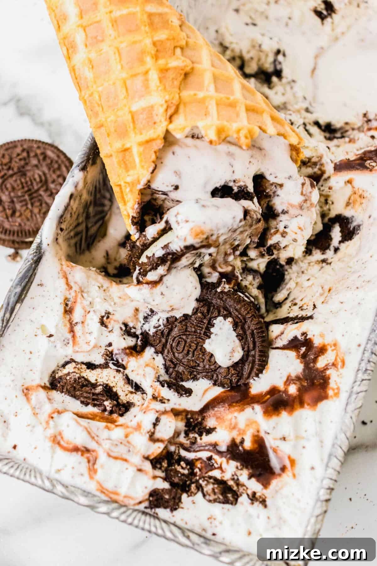 Oreo Cookie Bliss 2 An ice cream cone is digging into a container of Oreo ice cream, showcasing its rich texture and generous cookie chunks.