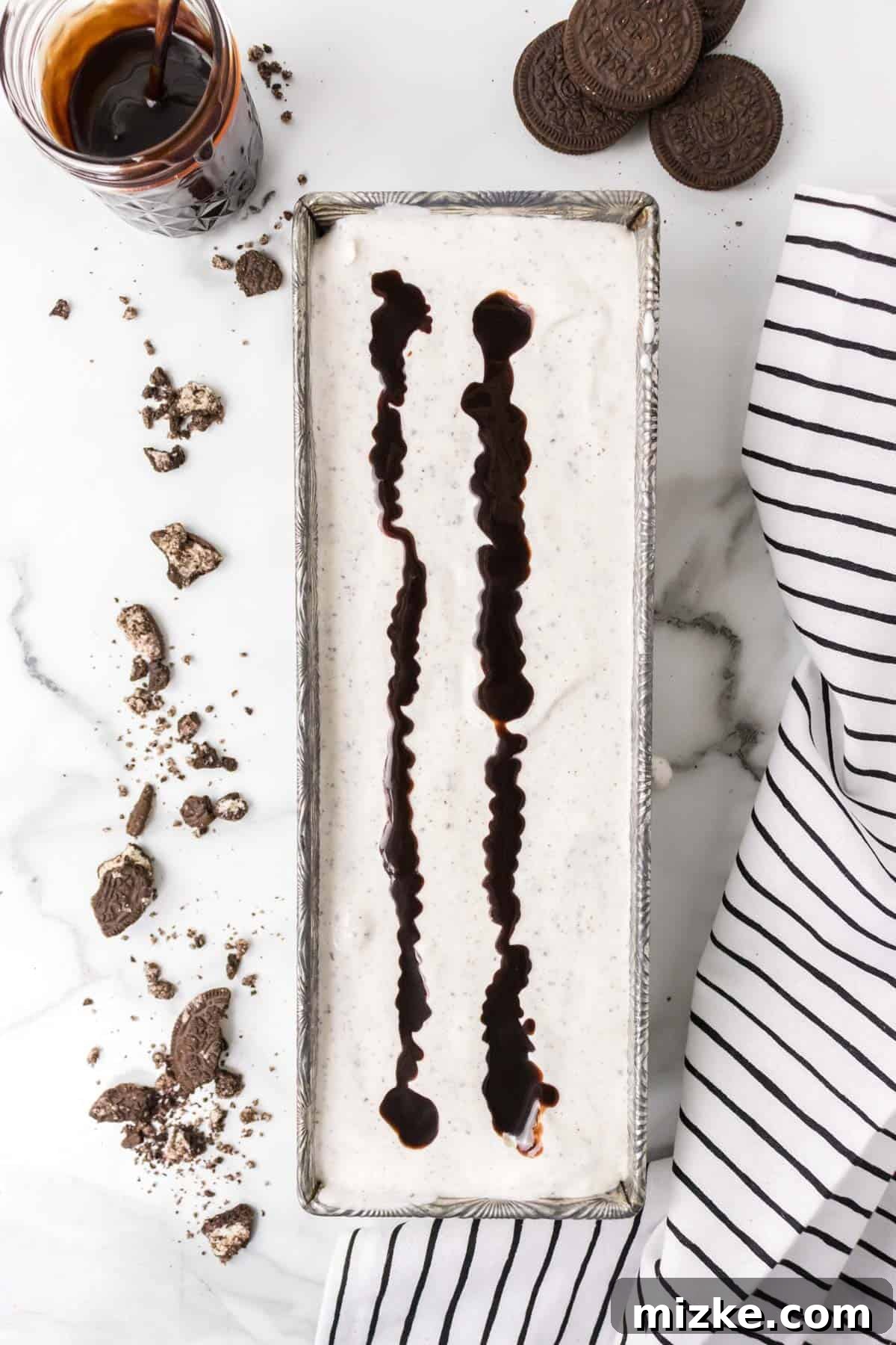 Oreo Cookie Bliss 9 Two generous lines of hot fudge topping drizzled over the smooth ice cream base in a container, ready for swirling.