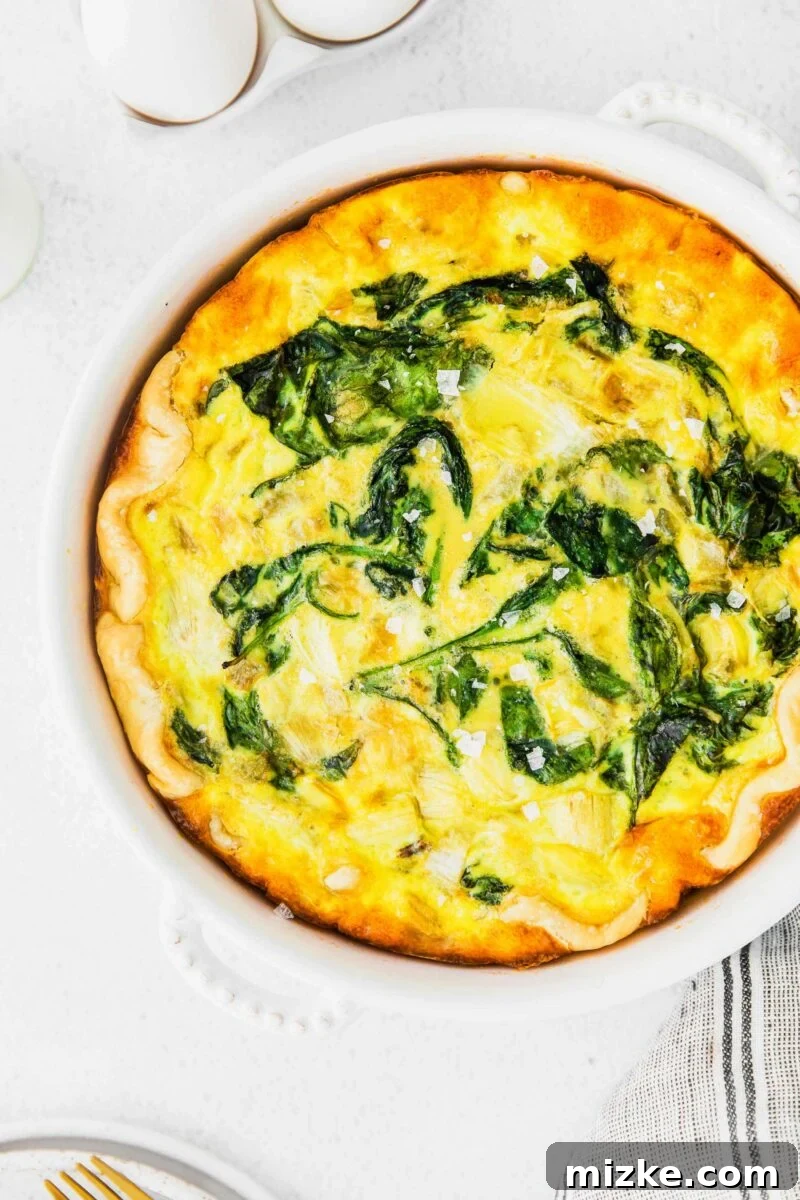 Savory Spinach and Artichoke Quiche 2 A freshly baked Spinach and Artichoke Quiche, garnished with flaky sea salt, sits on a rustic wooden board.