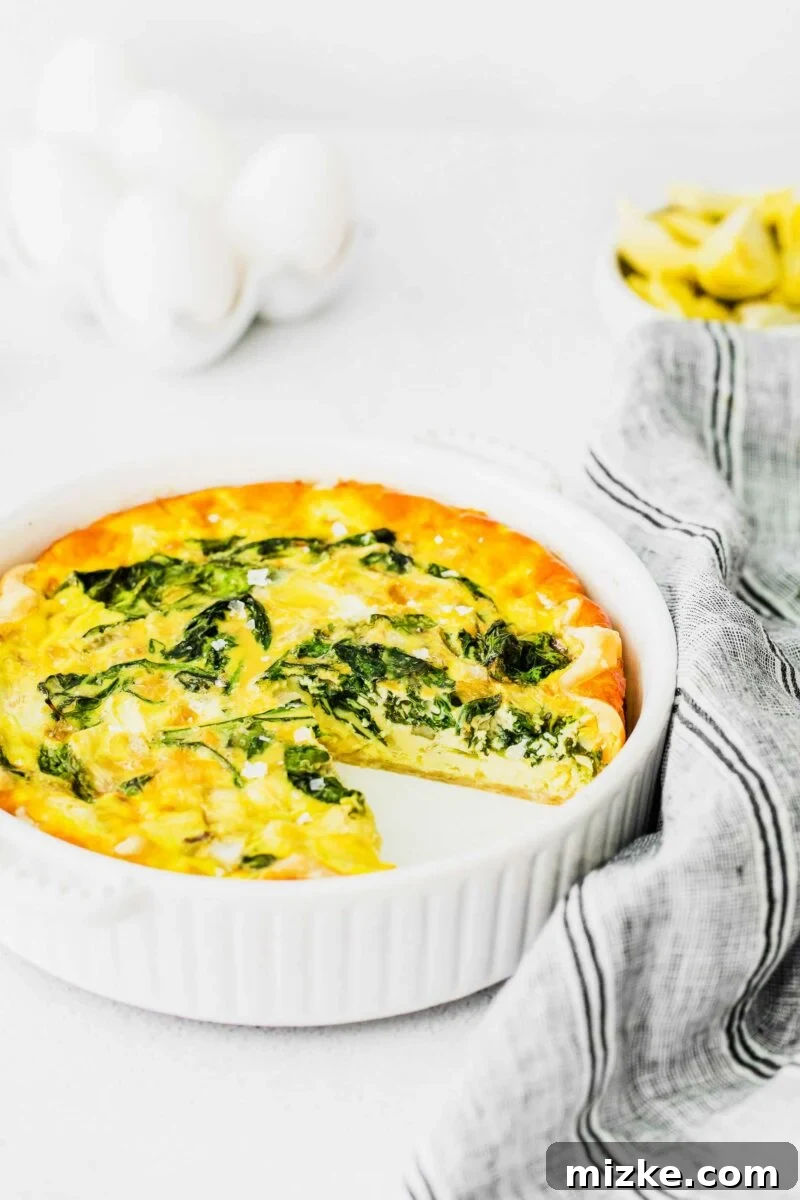 Savory Spinach and Artichoke Quiche 4 A white ceramic baking dish holds a Spinach and Artichoke Quiche with one slice already removed, showcasing the generous filling.