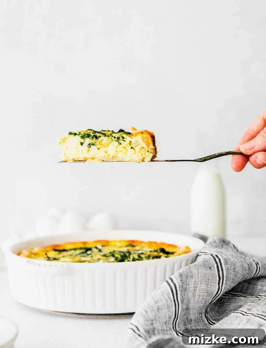 Savory Spinach and Artichoke Quiche 5 A slice of golden-brown quiche is being lifted from the pan with a serving spatula, steam gently rising.