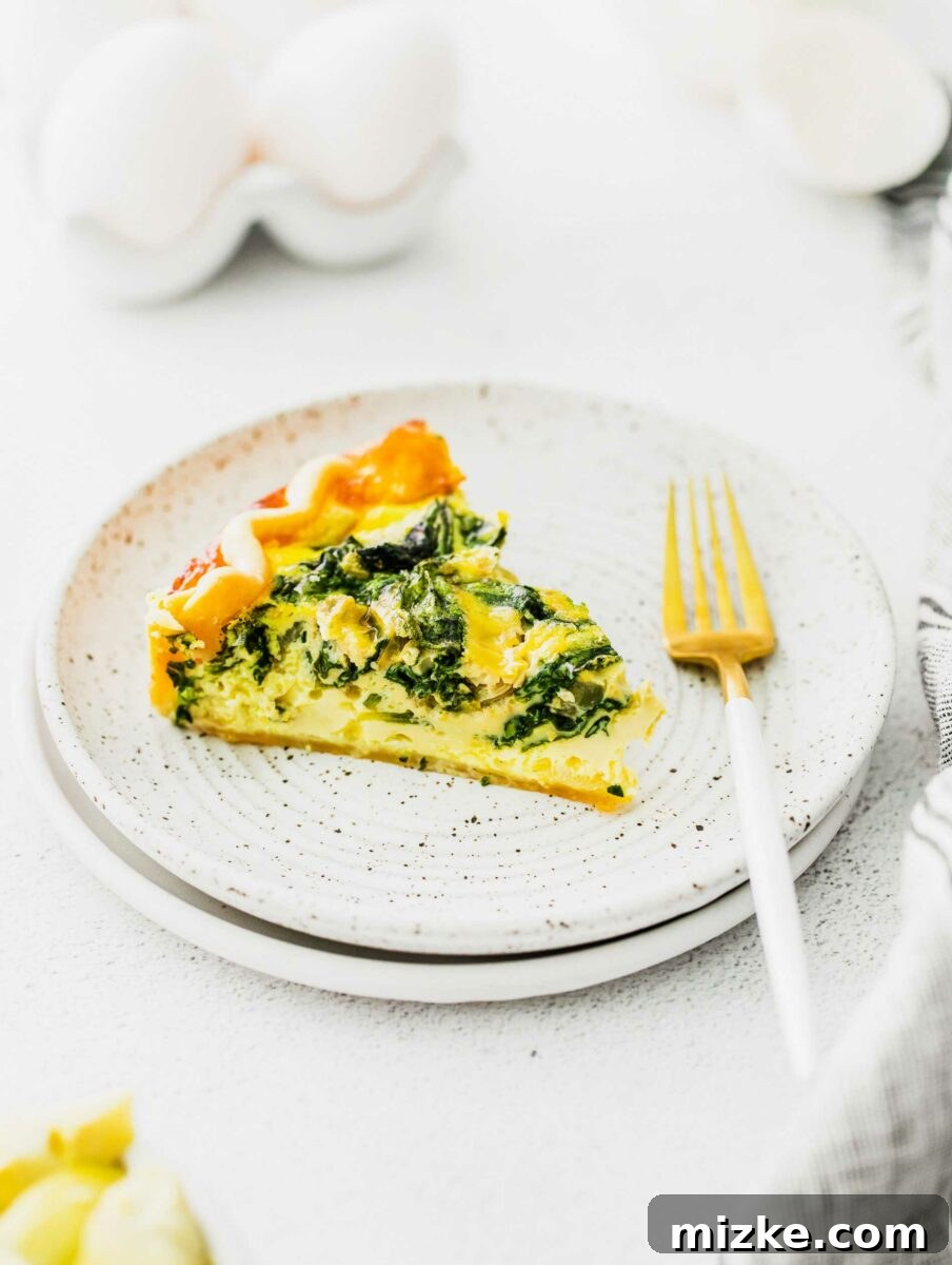 Savory Spinach and Artichoke Quiche 6 A single slice of Spinach and Artichoke Quiche on a white plate with a fork resting beside it, inviting a bite.
