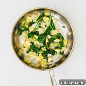 Savory Spinach and Artichoke Quiche 9 Spinach and artichoke mixture cooking in a metal skillet with onions and garlic.