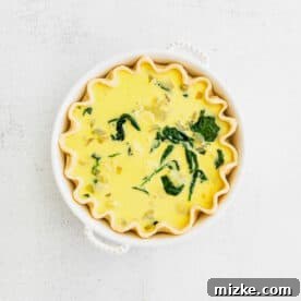 Savory Spinach and Artichoke Quiche 10 Egg custard being poured over spinach, artichoke, and cheese mixture in a pie crust.
