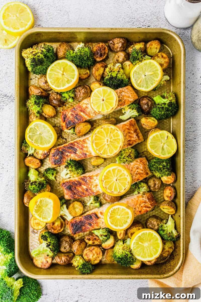 Salmon filets, lemon slices, potatoes and broccoli are spread out on a baking sheet. 