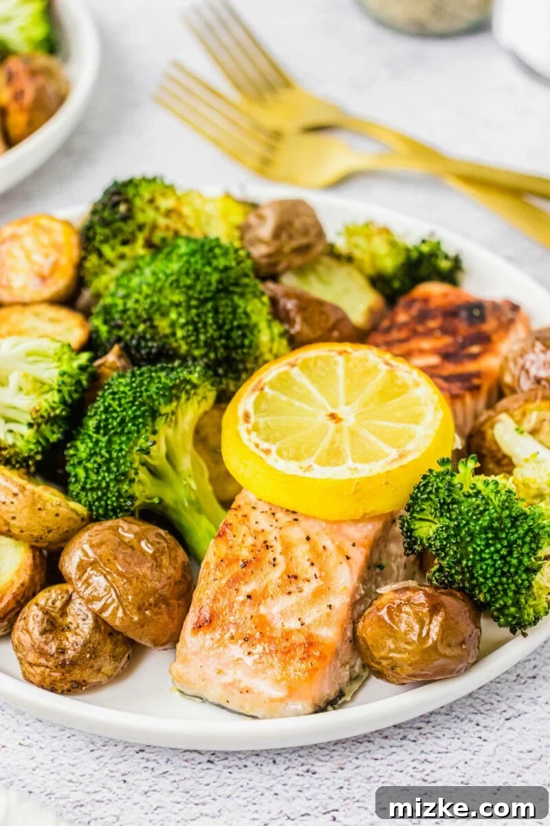 A lemon slice is placed upon a baked salmon filet surrounded by veggies. 