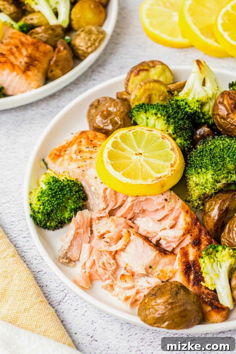 A salmon filet has been broken apart by a fork on a white plate. 