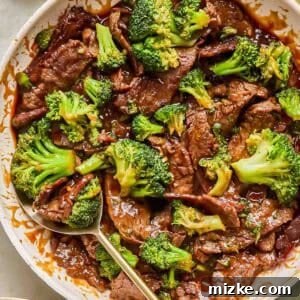 A skillet filled with teriyaki beef and broccoli stir-fry, with a serving spoon and a bowl of white rice nearby.
