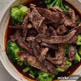 A skillet of cooked beef strips on top of steamed broccoli with a dark sauce.