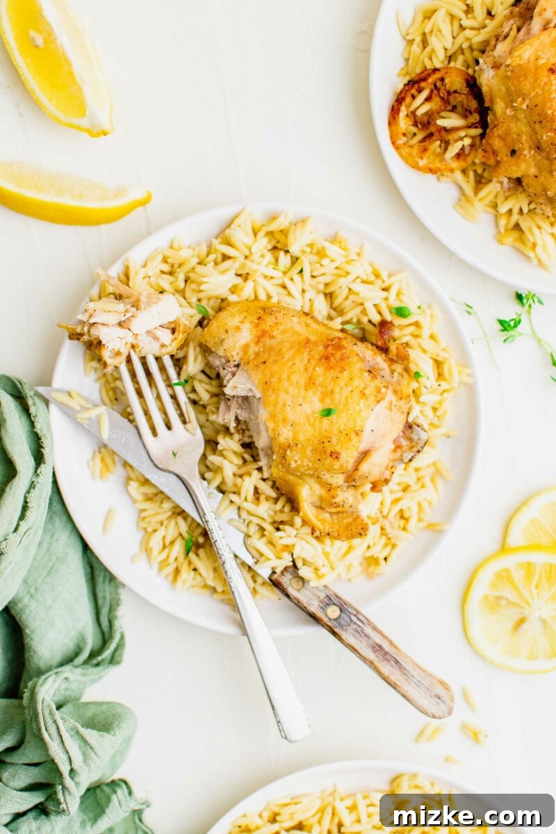 Zesty Lemon Garlic Chicken Orzo Skillet 6 A fork and knife placed neatly beside a plate piled high with creamy garlic lemon chicken orzo, ready to be enjoyed.