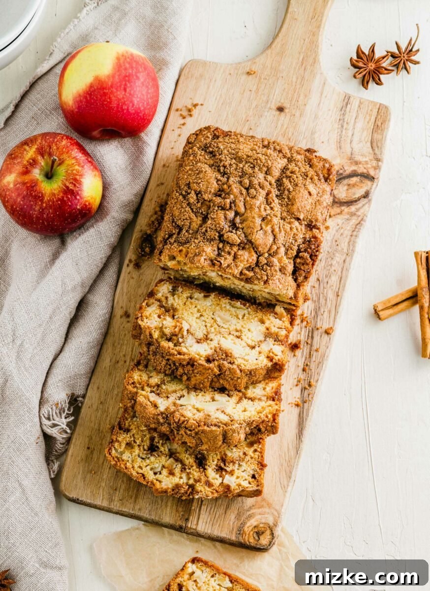 A freshly baked loaf of apple cinnamon swirl bread is being sliced on a rustic wooden cutting board, revealing the beautiful cinnamon and apple swirl within.