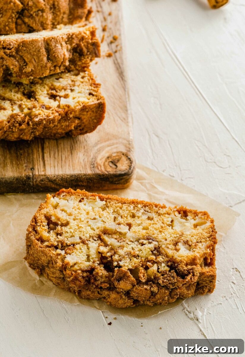 A perfect slice of apple cinnamon swirl bread is displayed on a crisp white surface, showcasing the intricate cinnamon pattern and moist crumb.