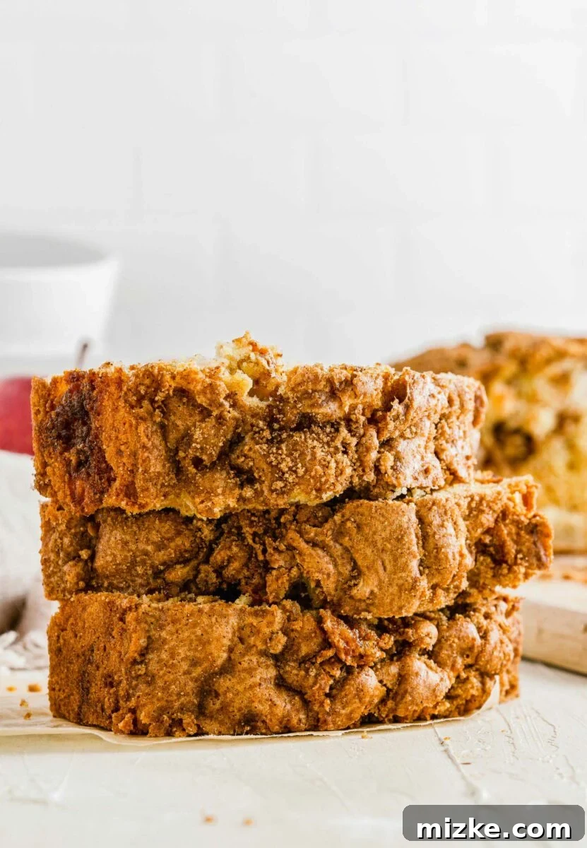 Three perfectly cut slices of apple cinnamon swirl bread are stacked on a pristine white surface, highlighting their delicious layers.