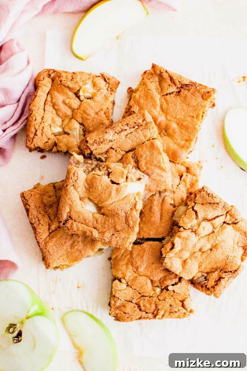 Spiced Apple Blondies 2 Handheld squares of apple blondies are placed on a white surface next to green apple slices.