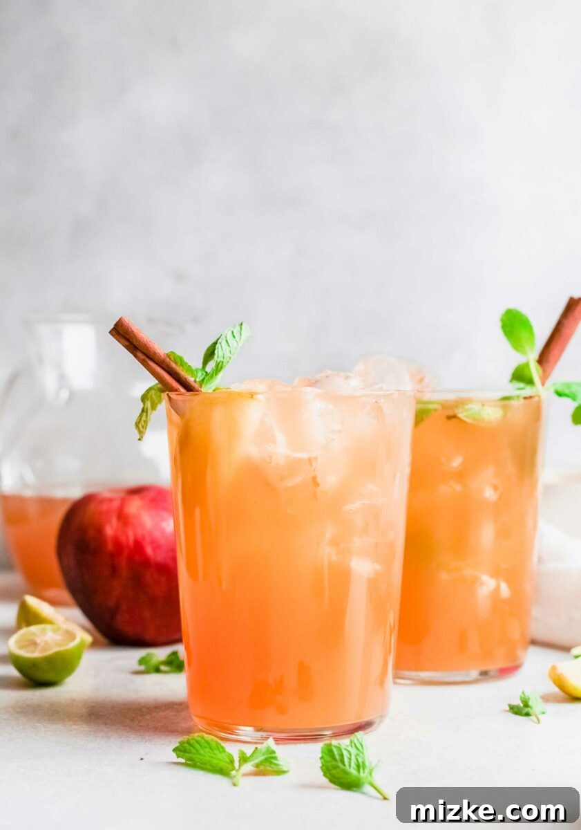 Crisp Apple Mojito 5 Two glasses of mojito are placed next to an apple, mint sprigs, and lime halves, highlighting fresh ingredients.