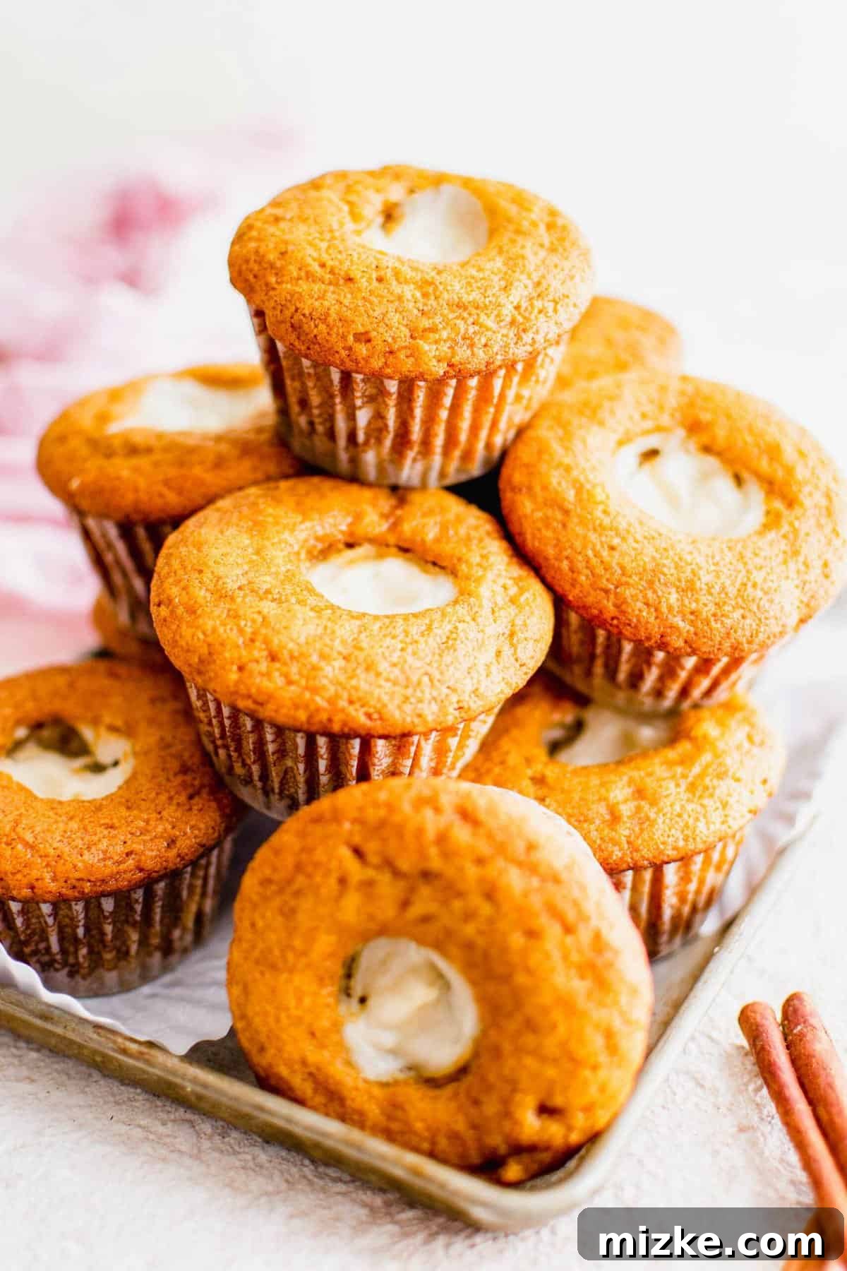 These Starbucks copycat pumpkin cream cheese muffins are soft, moist, and filled with gooey cream cheese and spice. Perfect for fall baking! A carefully arranged stack of golden-brown pumpkin cream cheese muffins on a pristine white surface, ready to be enjoyed.