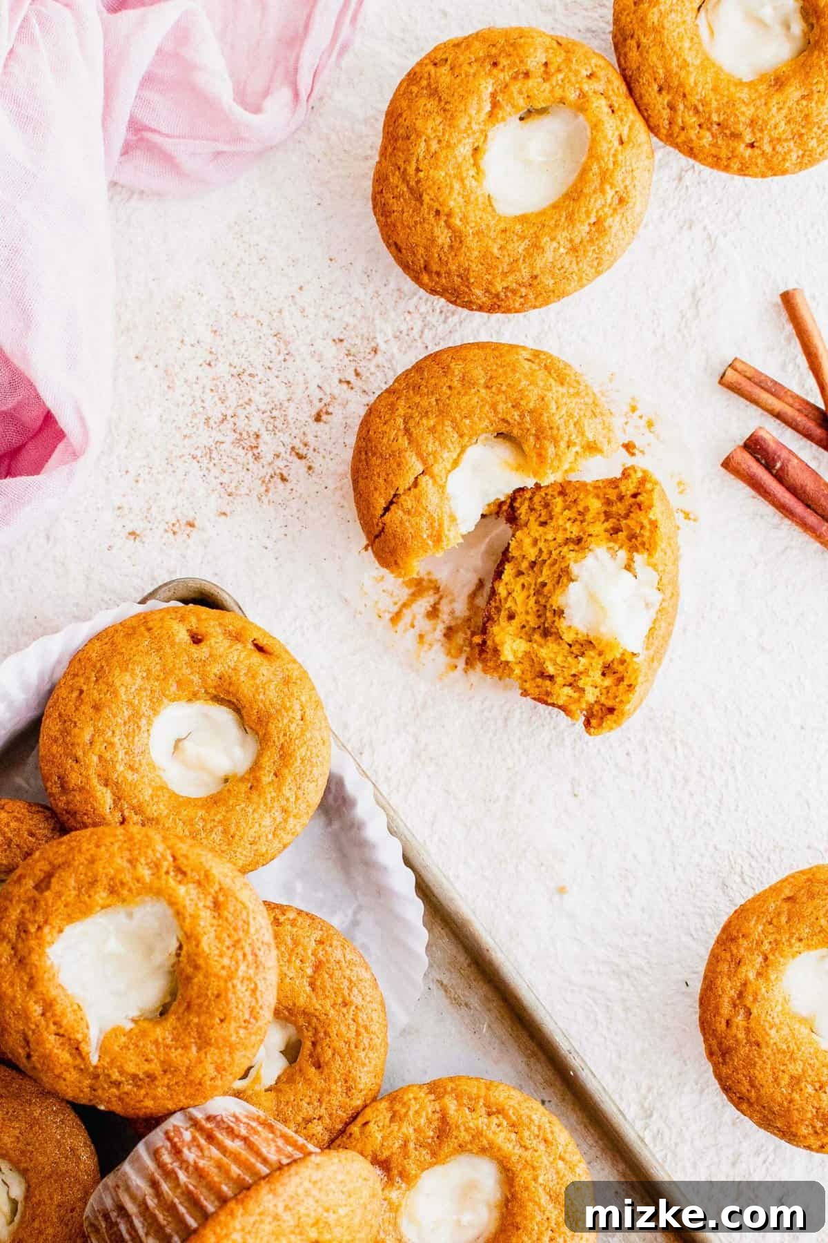 These Starbucks copycat pumpkin cream cheese muffins are soft, moist, and filled with gooey cream cheese and spice. Perfect for fall baking! A beautiful arrangement of freshly baked pumpkin cream cheese muffins artfully displayed with aromatic cinnamon sticks.