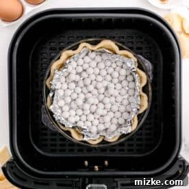 Air Fryer Pumpkin Perfection 4 A pie crust with tin foil and pie weights placed inside the basket of an air fryer for blind baking.
