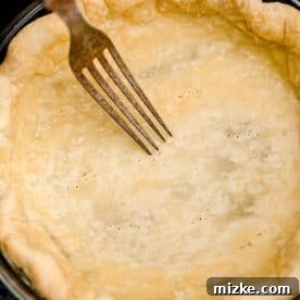 Air Fryer Pumpkin Perfection 5 A fork is gently piercing the bottom of a partially baked pie crust.