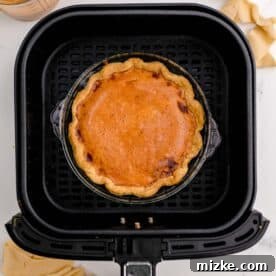 Air Fryer Pumpkin Perfection 8 A perfectly baked pumpkin pie resting in an air fryer basket, with a golden-brown crust and set filling.