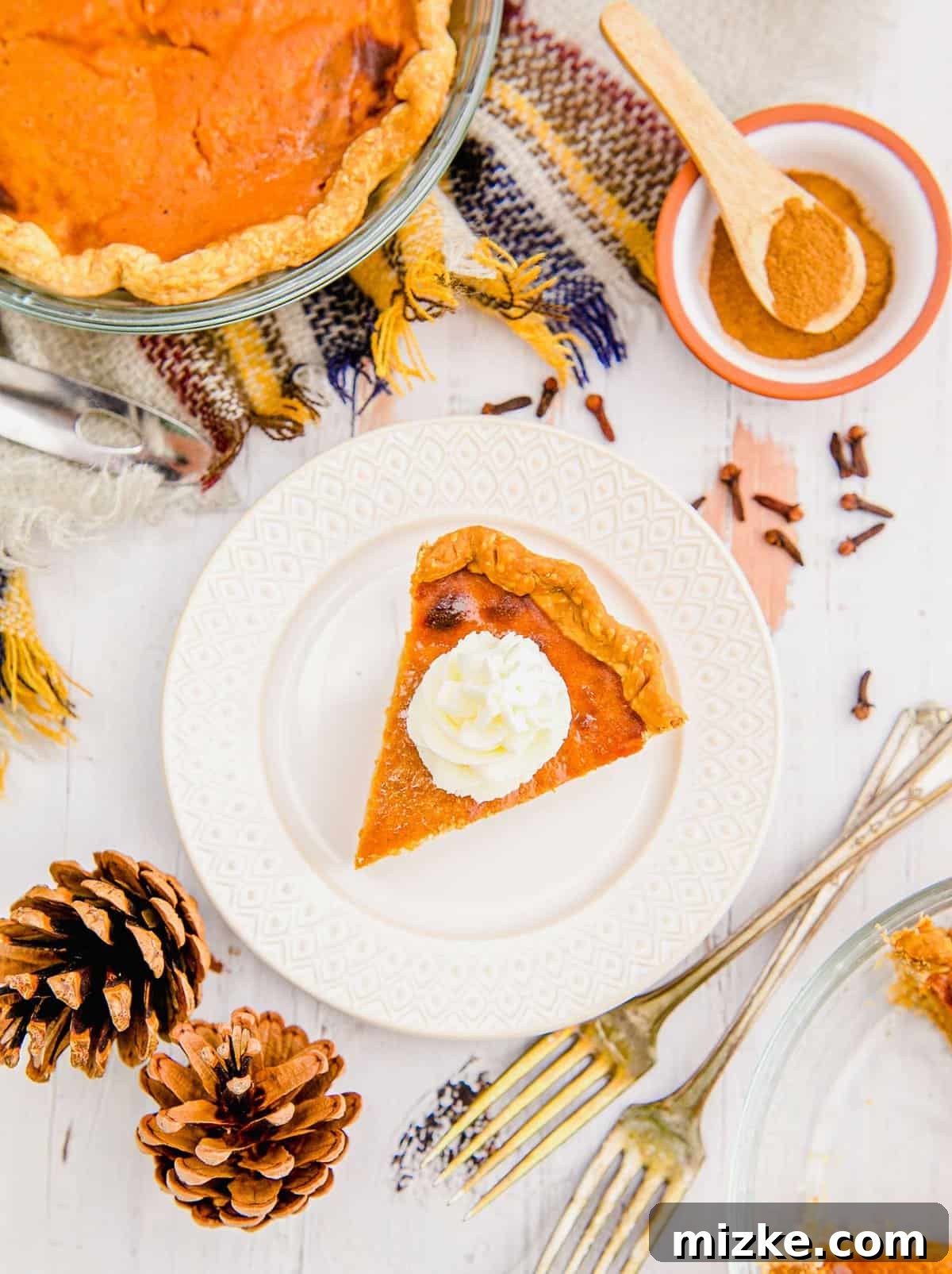 Air Fryer Pumpkin Pie with Fall Decor A beautifully crafted slice of air fryer pumpkin pie, elegantly presented with autumn pinecones and forks.