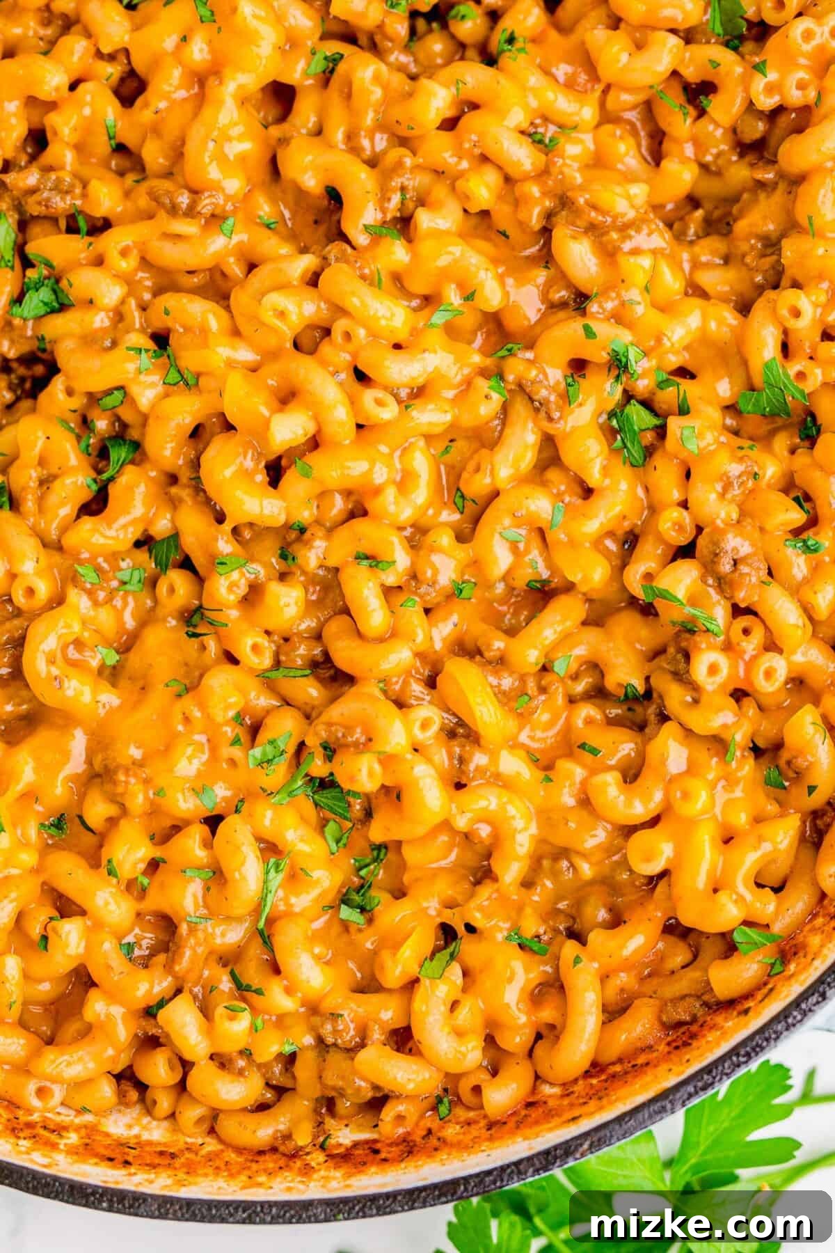Cheesy noodles and ground beef are garnished with fresh parsley, served in a cast iron skillet.