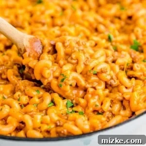 A wooden spoon scoops up cheesy pasta from a cast iron skillet, showcasing the rich texture of the dish.