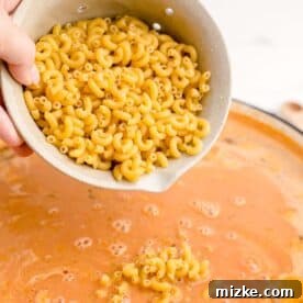 Dried elbow macaroni pasta is being added to a cast iron skillet filled with savory beef and sauce.