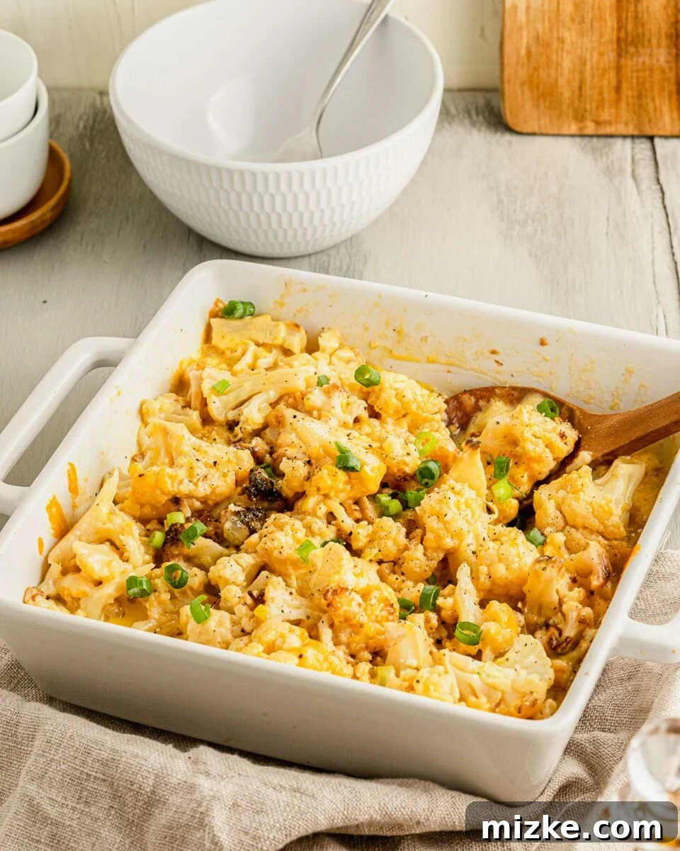 Golden Baked Cheesy Cauliflower Delight 2 A wooden spoon is placed in a white square casserole dish filled with baked cauliflower and cheese.