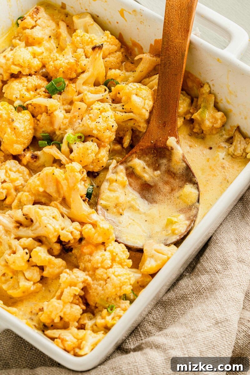 Golden Baked Cheesy Cauliflower Delight 5 A wooden spoon is placed in a dish filled with cheesy baked cauliflower.
