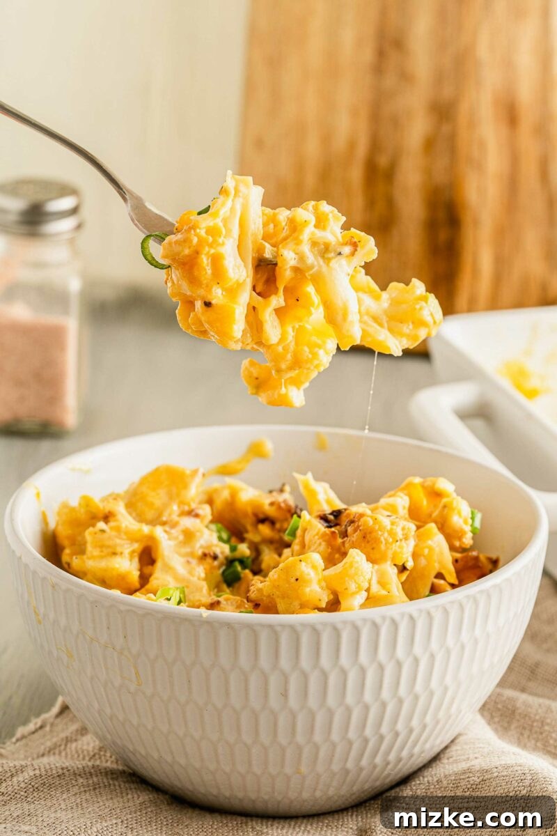 Golden Baked Cheesy Cauliflower Delight 7 A fork is lifting a bite of cauliflower from a white bowl.