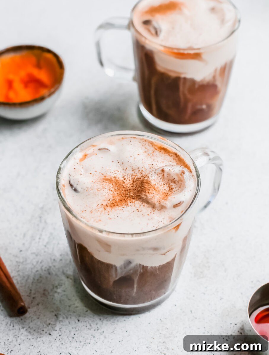 Starbucks Inspired Pumpkin Cream Cold Brew 5 A hand pouring foamy pumpkin cream into a glass filled with cold brew coffee and ice, illustrating the final step of making the drink.