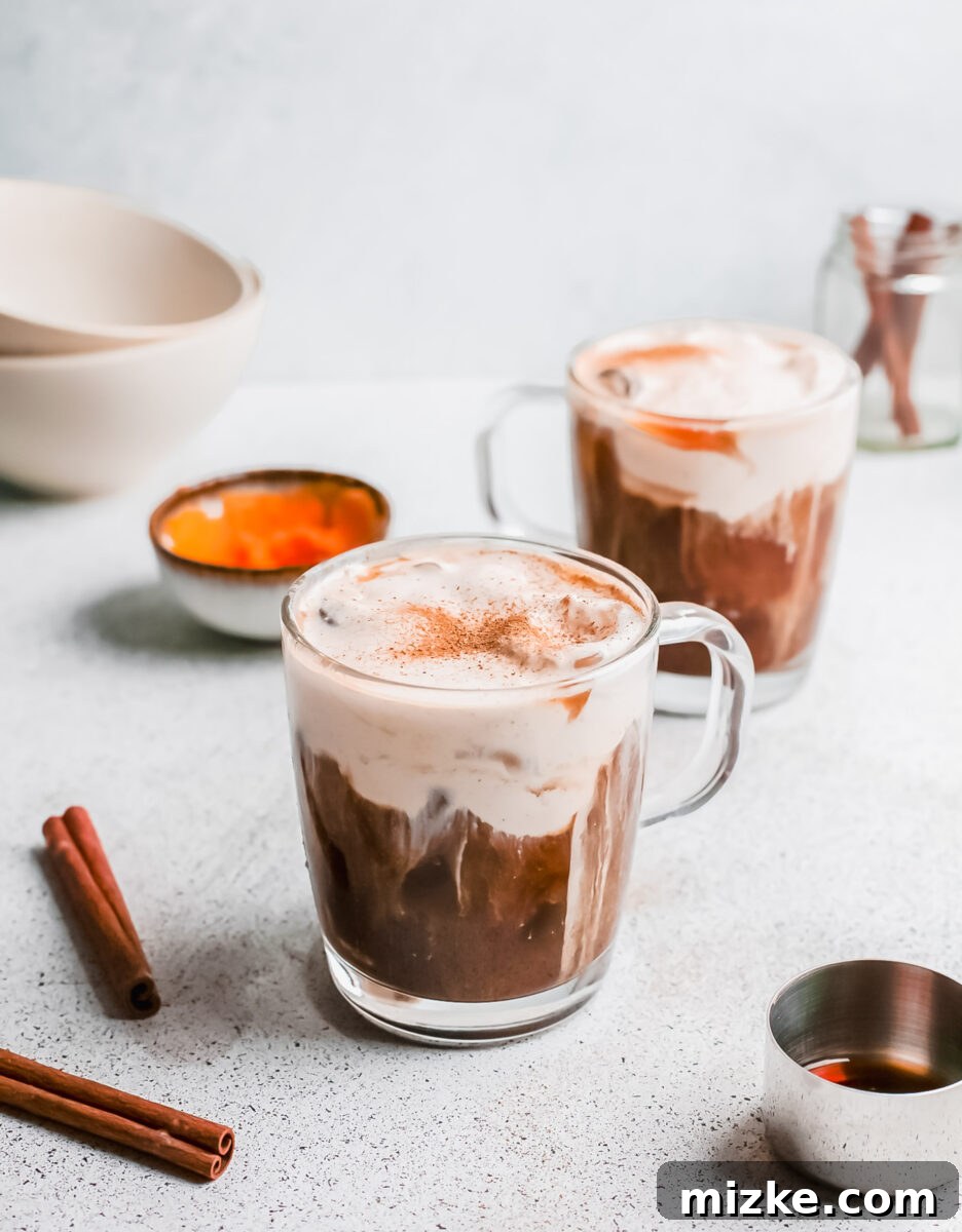 Starbucks Inspired Pumpkin Cream Cold Brew 6 Two glasses of homemade Pumpkin Cream Cold Brew, garnished with pumpkin pie spice, positioned on a wooden surface, ready to be enjoyed.