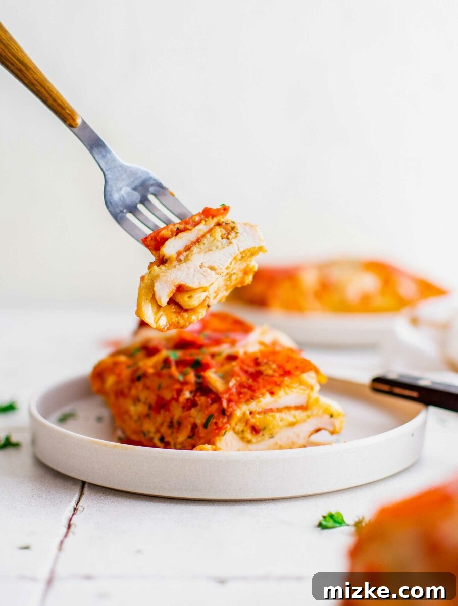 Pizza Bomb Chicken 6 A bite of pizza stuffed chicken is being lifted from a white plate.