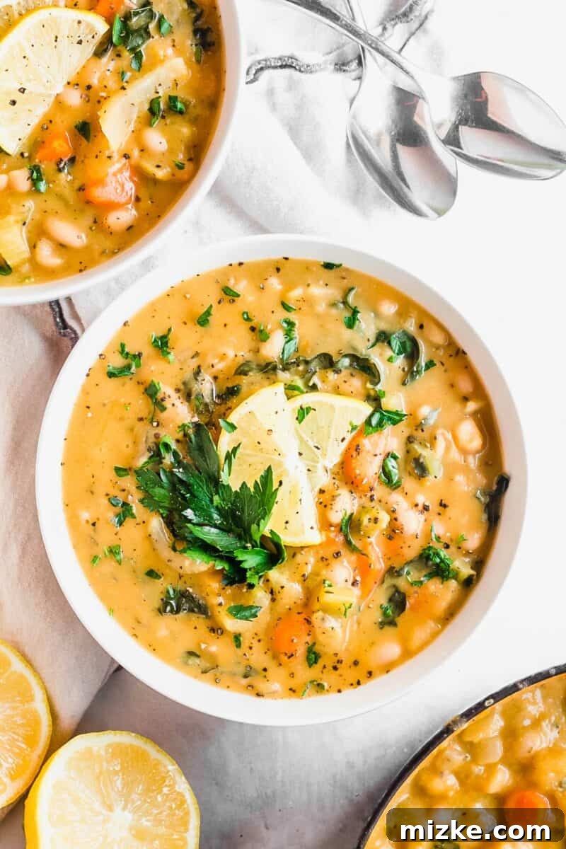 Plant-Based White Bean Comfort Stew 2 Several garnished bowls of white bean soup are placed on a white surface, invitingly warm.