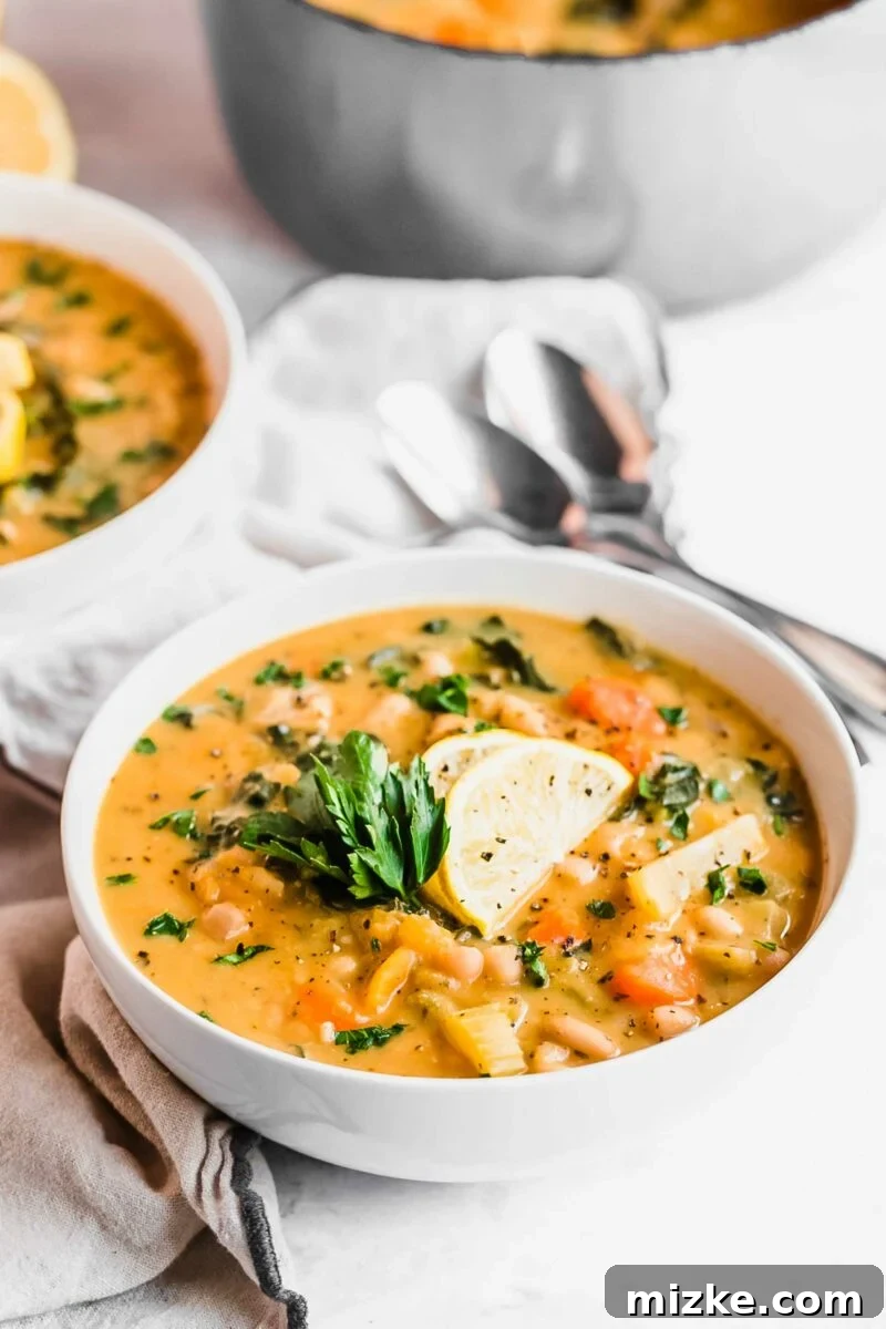 Plant-Based White Bean Comfort Stew 4 A white bowl is filled with rich vegan soup, beautifully garnished with fresh parsley and two bright slices of lemon.