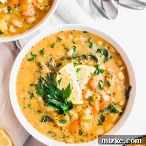 A top-down view of the Cozy Vegan White Bean Soup, garnished with fresh parsley and a lemon slice.
