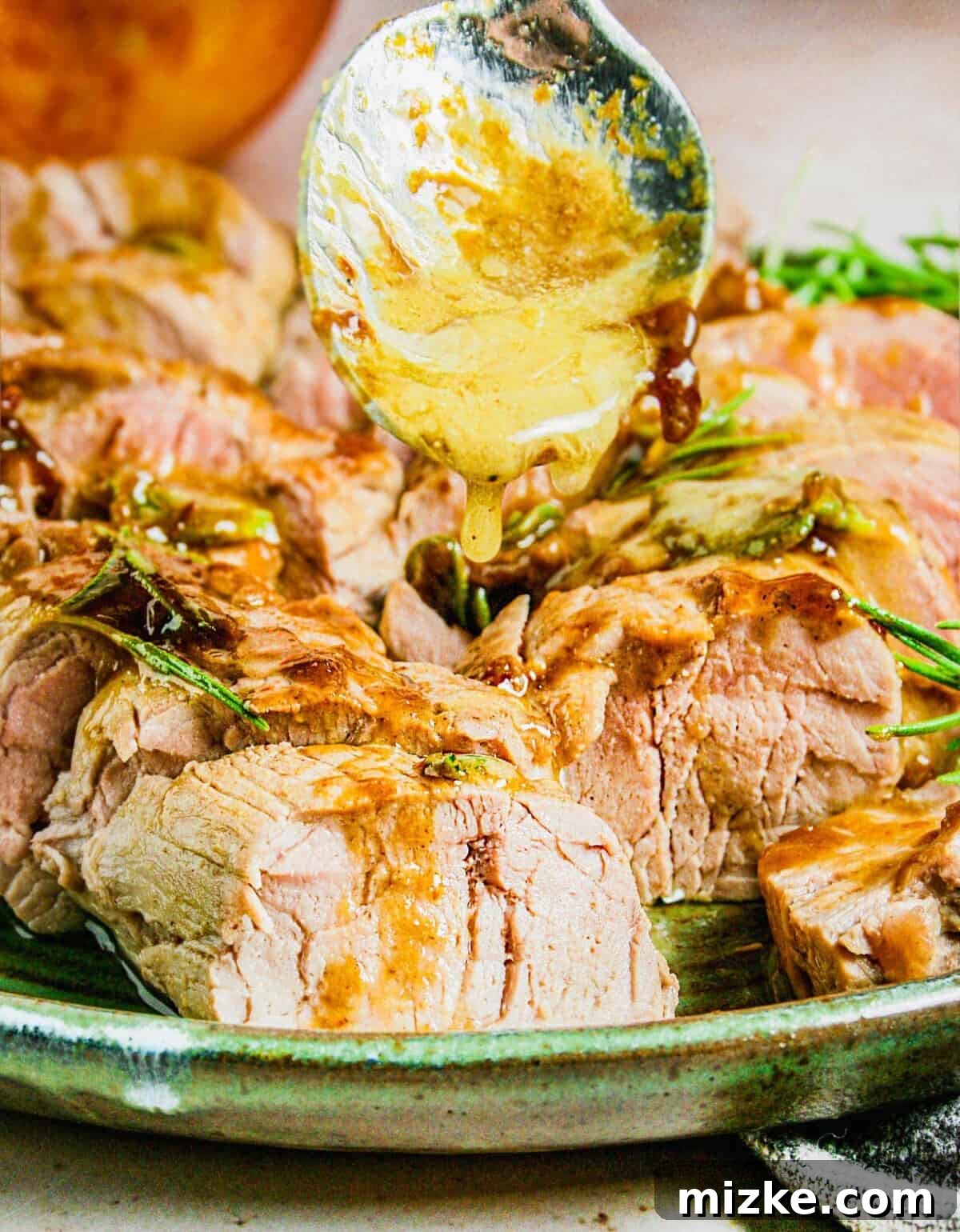 Maple-Glazed Mustard Pork Tenderloin 2 A spoon is drizzling golden brown glaze on a piece of pork.
