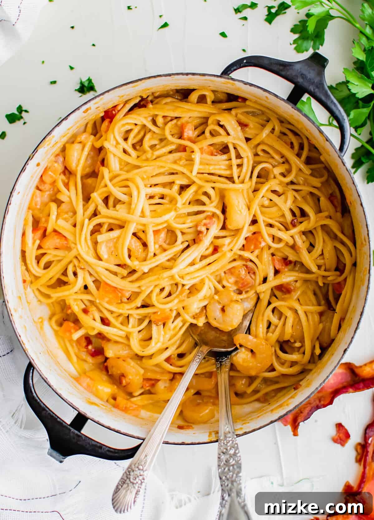 Spicy Cajun Shrimp Skillet Pasta 2 A large pot brimming with creamy Cajun shrimp pasta, garnished with fresh parsley. A metal serving fork and spoon rest beside it, inviting you to dive in.