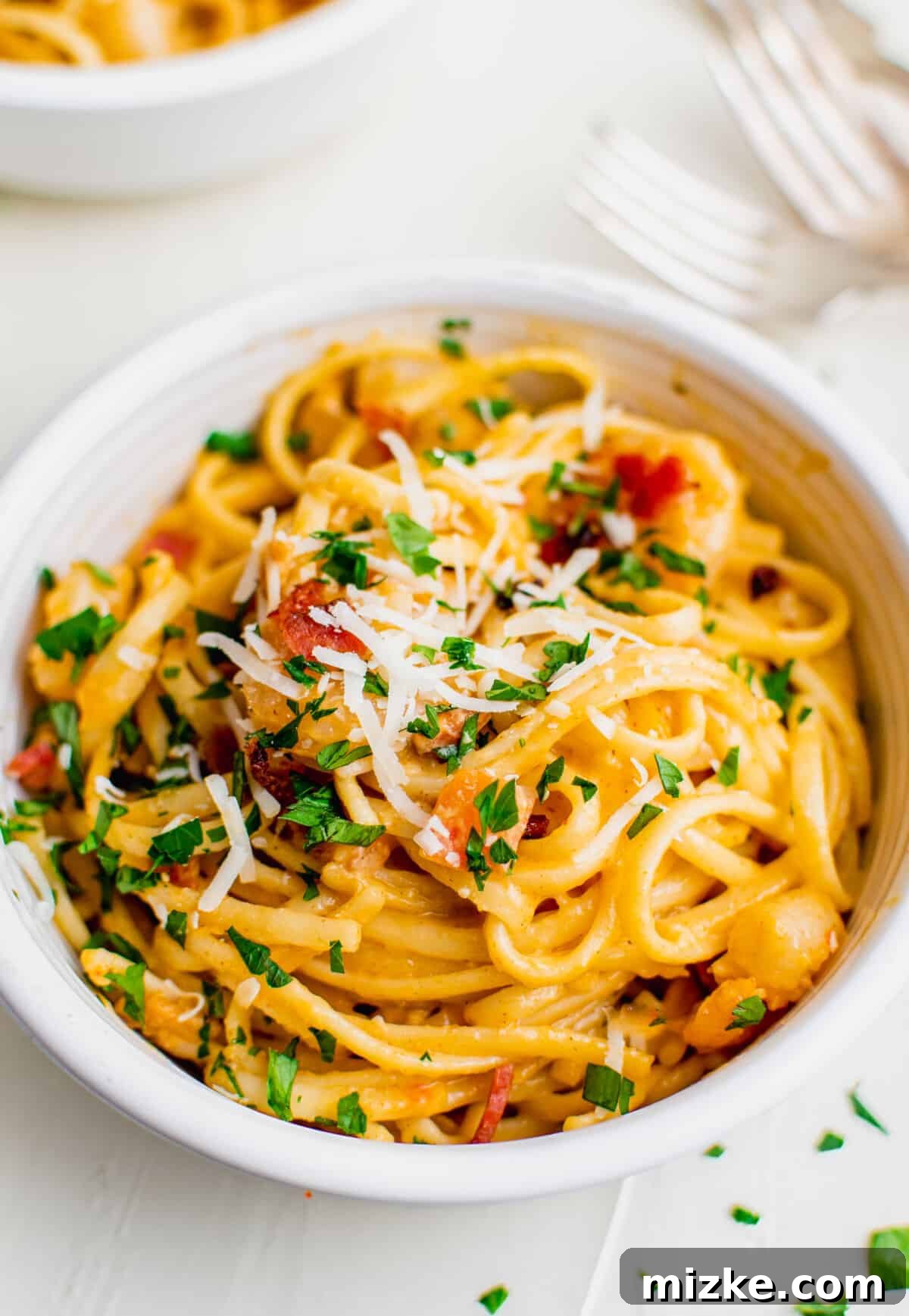 Spicy Cajun Shrimp Skillet Pasta 3 A white bowl filled with Cajun shrimp pasta, elegantly topped with fresh parsley, a sprinkle of grated Parmesan cheese, and crispy bacon pieces.