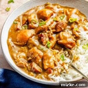 A bowl of chicken and sausage gumbo, garnished with fresh green onions, served with a side of white rice. The dish is presented beautifully on a light surface with a blue napkin, inviting a delicious meal.
