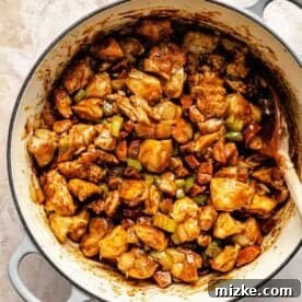 Hearty Chicken and Sausage Gumbo 10 A large pot filled with browned chicken and sausage, along with sautéed vegetables, is mixed with the rich dark roux using a wooden spoon, creating a cohesive and flavorful base for the gumbo on a marbled surface.