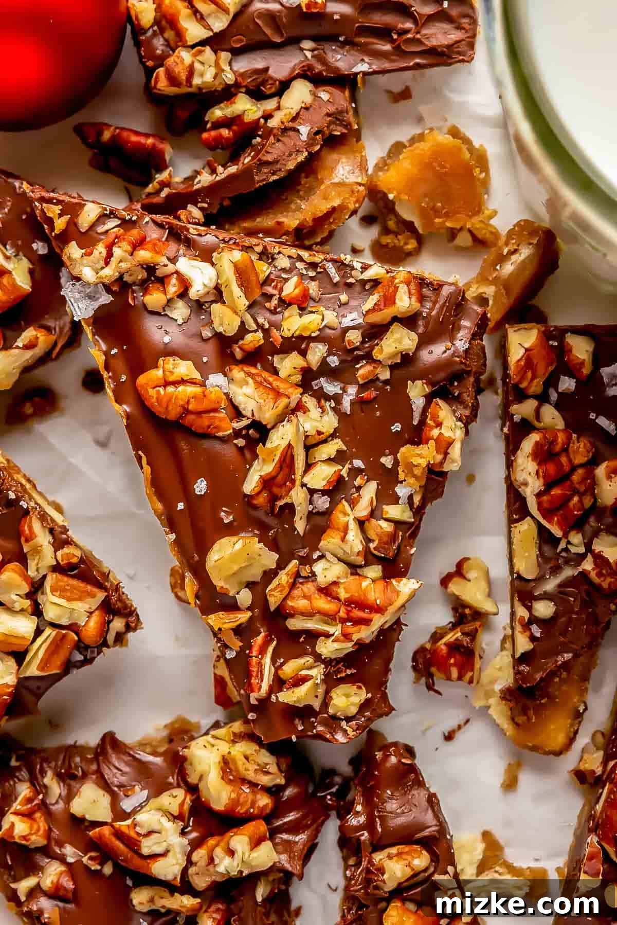 Golden Saltine Caramel Crunch 3 A perfectly triangular piece of saltine toffee, adorned with finely chopped pecans and a sprinkle of flakey sea salt, captured in close-up detail