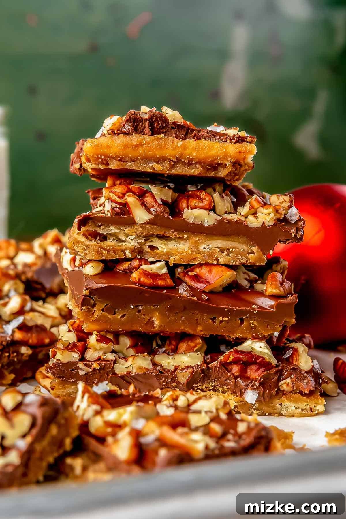 Golden Saltine Caramel Crunch 4 Several pieces of saltine toffee stacked neatly on top of one another on a baking sheet, displaying their golden caramel and dark chocolate layers with scattered pecan pieces