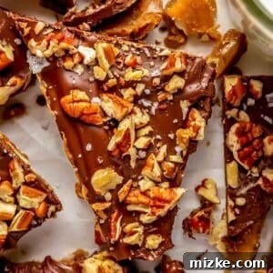 A close-up of a triangular saltine toffee piece, garnished with chopped pecans and sea salt.