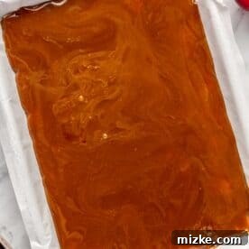The molten butter and brown sugar mixture being carefully poured over the saltine crackers on the baking sheet, ready for baking
