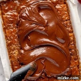 Melted chocolate being smoothly spread over the cooled caramel layer on the saltine crackers, creating an even topping