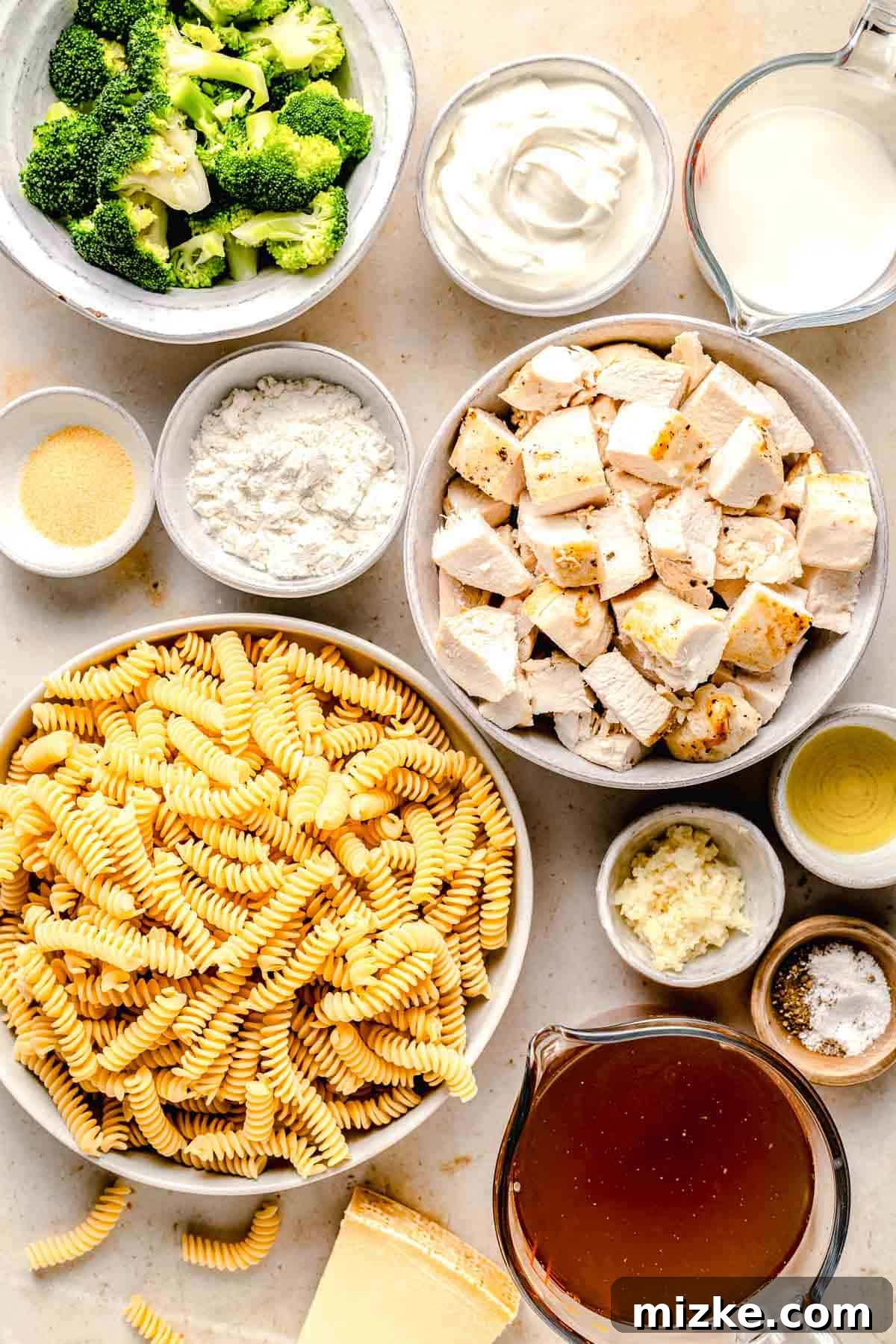 Key ingredients for Chicken Broccoli Alfredo pasta: rotini, chicken, broccoli, fresh garlic, olive oil, and dairy products for the creamy sauce. Fresh ingredients laid out on a wooden cutting board, including rotini pasta, broccoli florets, cubed chicken, garlic, olive oil, milk, and Greek yogurt, ready for making Chicken Broccoli Alfredo.