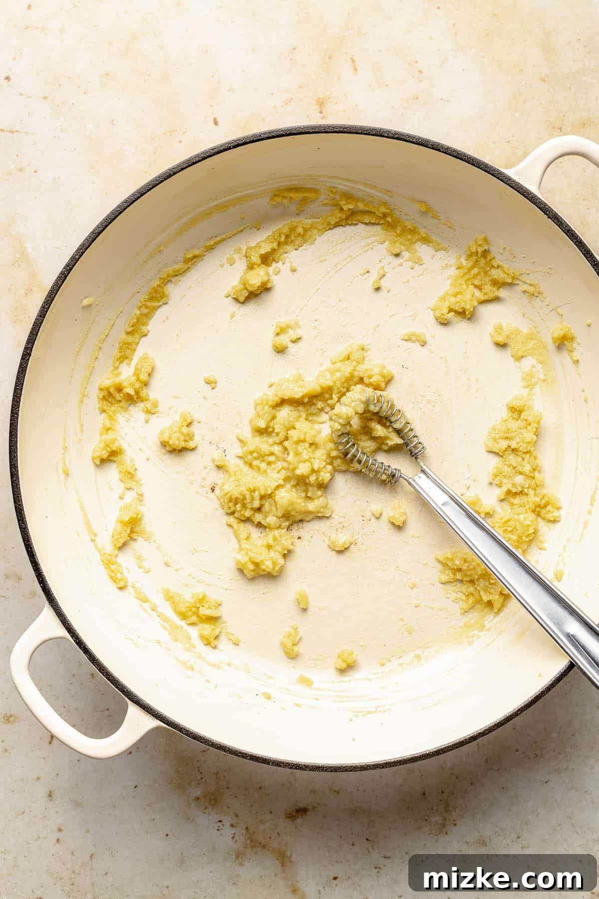 Making the garlic-infused roux for a homemade Alfredo sauce. Sautéing minced garlic in olive oil in a large skillet to form the base of the Alfredo sauce roux.